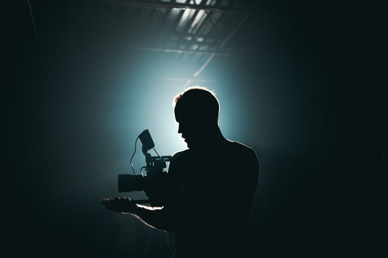 about-01 Silhouette of a cinematographer with camera gear in a dramatic, low light setting.